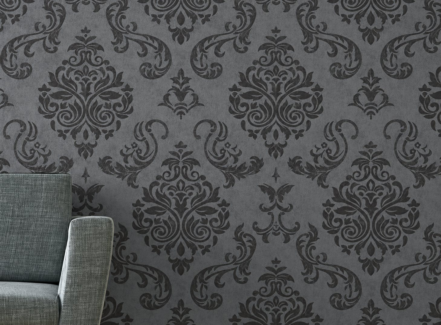 Un mur recouvert de papier peint gris anthracite à motifs baroques, devant lequel se trouve un fauteuil en tissu gris vert.
